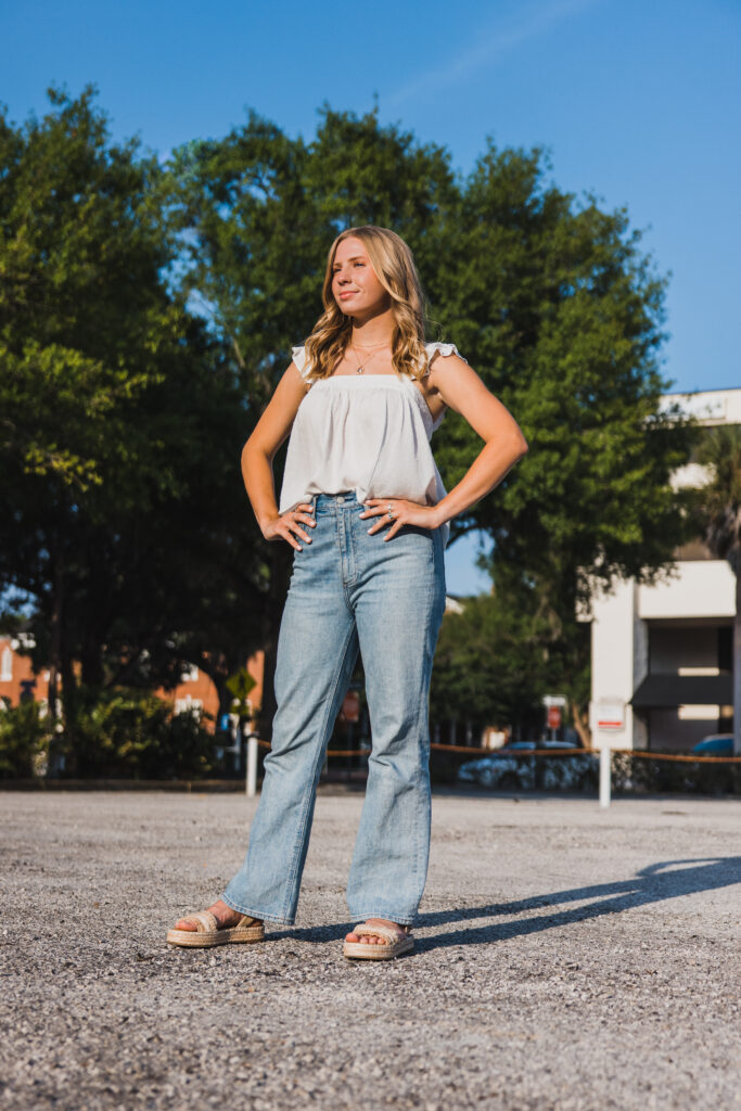 Image of a high school senior posing in a natural setting with a relaxed smile and a casual outfit, standing in the sun. 