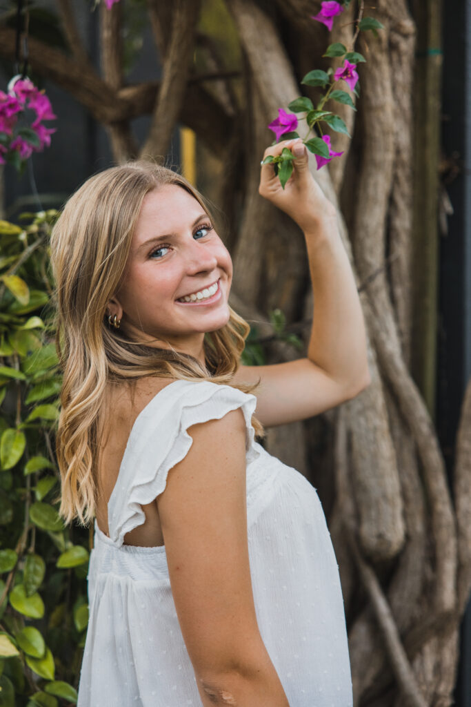 Image of a high school senior posing in a natural setting with a relaxed smile and a casual outfit, holding flowers. 