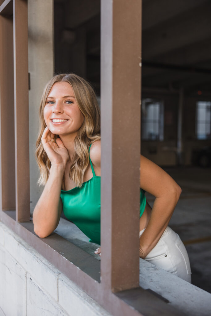 Image of a high school senior posing in a natural setting with a relaxed smile and a casual outfit, peeking out of a window. 