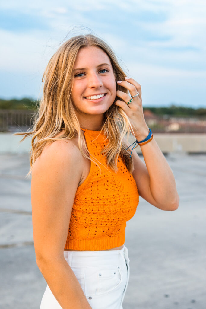 Image of a high school senior posing in a natural setting with a relaxed smile and a casual outfit, smiling with a blue sky. 
