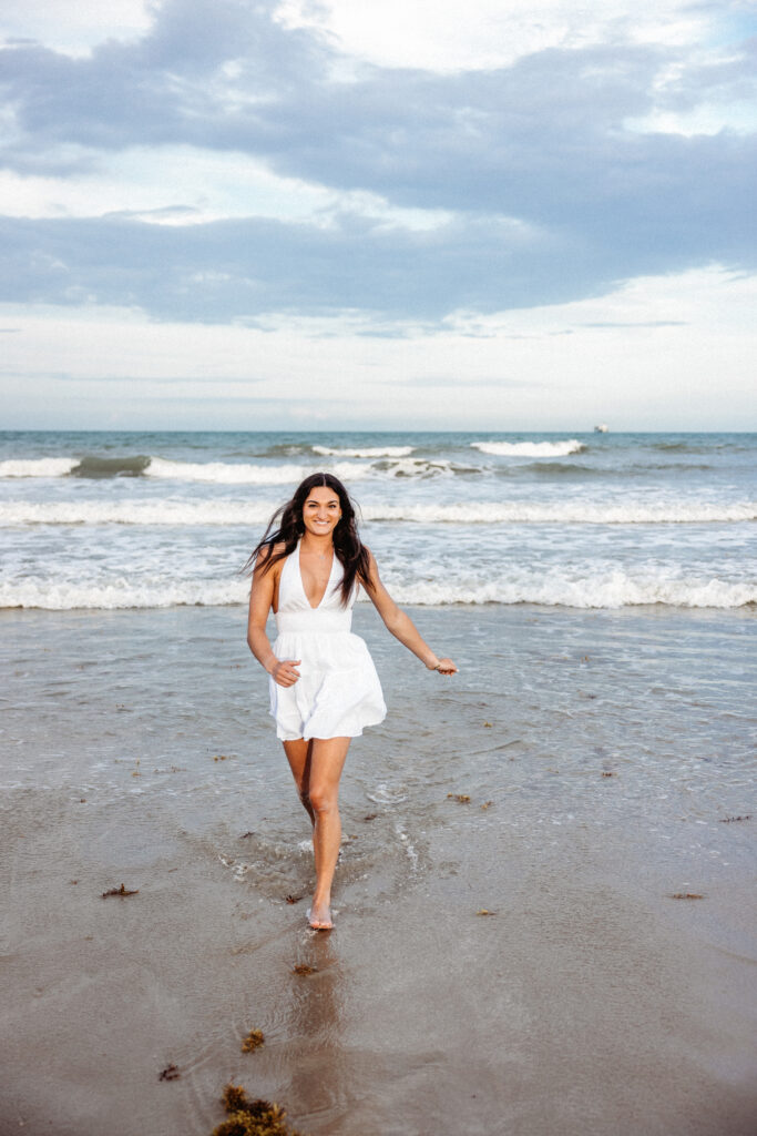 Image of a high school senior posing in a natural setting with a relaxed smile and a casual outfit, walking on the beach. 