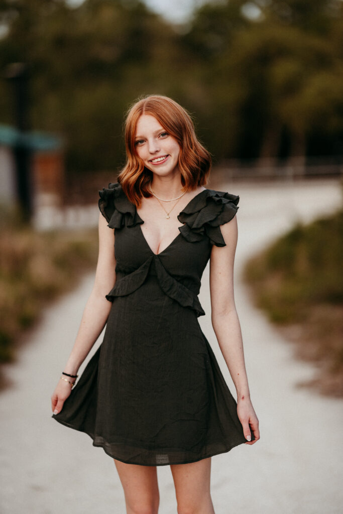 Image of a high school senior posing in a natural setting with a relaxed smile and a casual outfit, twirling on a path. 
