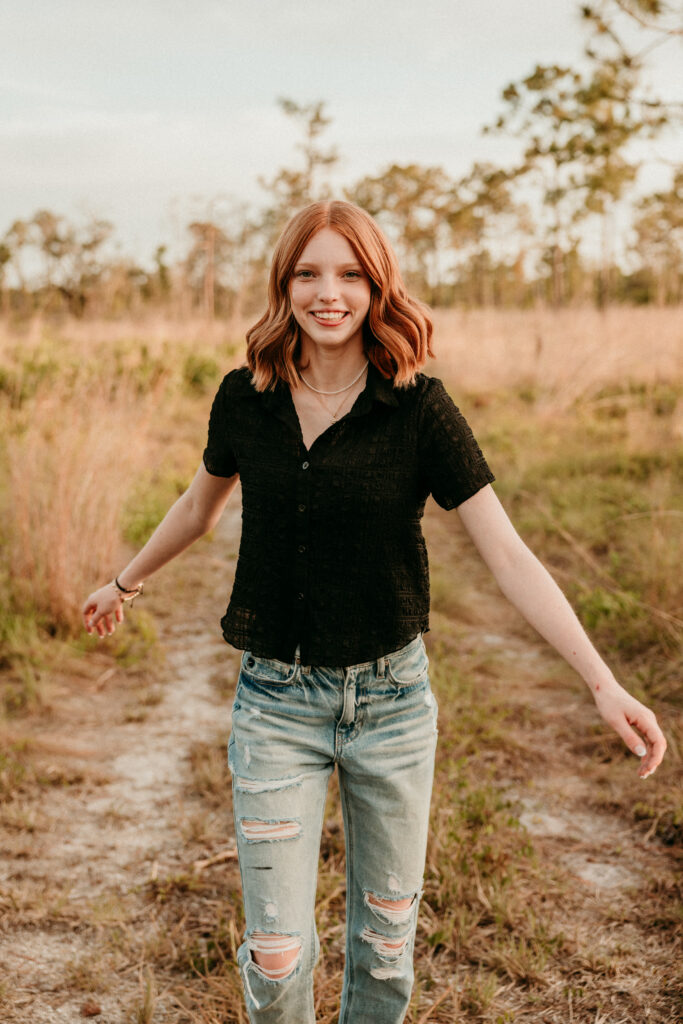 Image of a high school senior posing in a natural setting with a relaxed smile and a casual outfit, walking in a field. 
