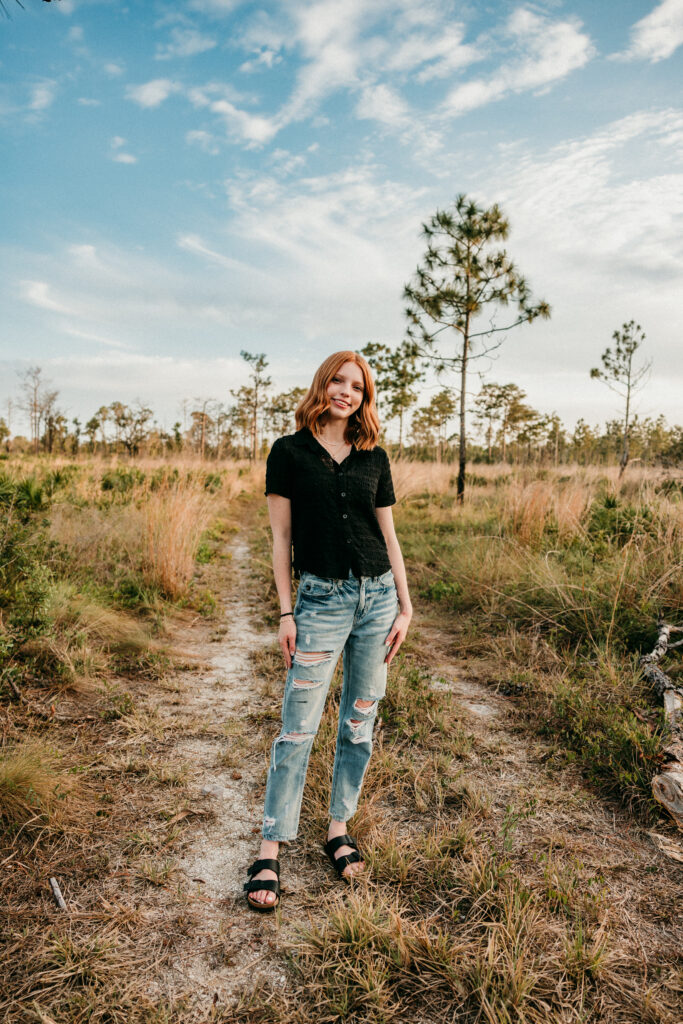 Image of a high school senior posing in a natural setting with a relaxed smile and a casual outfit, standing in a beautiful field. 