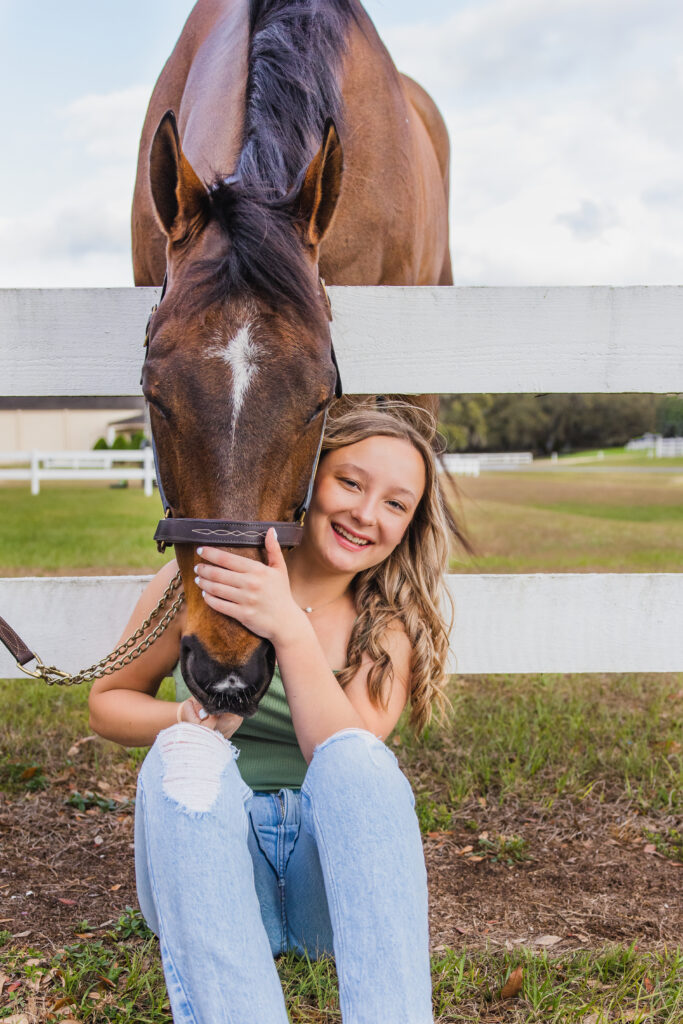 Image of a high school senior posing in a natural setting with a relaxed smile and a casual outfit, hugging her horse. 