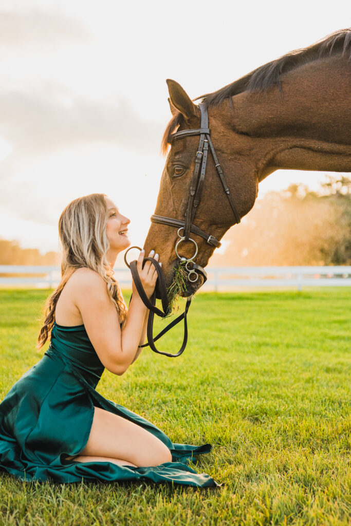 Image of a high school senior posing in a natural setting with a relaxed smile and a casual outfit, smiling at her horse. 