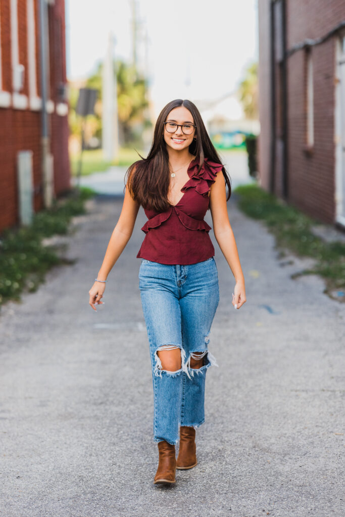 Image of a high school senior posing in a natural setting with a relaxed smile and a casual outfit, walking between buildings.